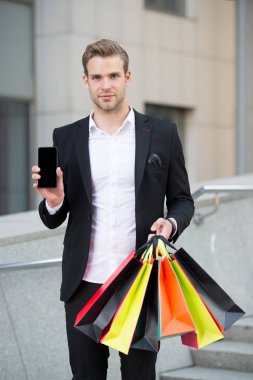 Online alışveriş. İşadamı kullanımı alışveriş uygulaması. Adam alışveriş torbaları tutun telefon kentsel arka planı süre taşır. Alışveriş online başarılı bir iş adamı. Online hizmet meşgul insanlar için teşekkür ederiz
