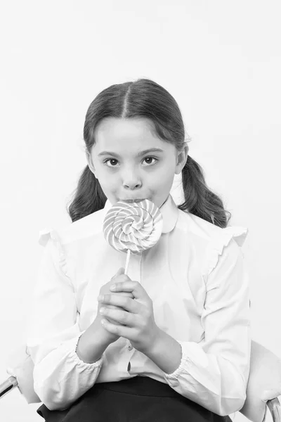 Vício em açúcar. Menina bonito garoto rabo de cavalo penteado comer pirulito doce. Doces em porções apropriadas ok. Menina aluna escola uniforme gosta de doces pirulito doce fundo amarelo. Seu sabor favorito — Fotografia de Stock