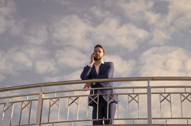 Patron konuşmak üstünde hareket eden telefon üzerinde mavi gökyüzü. Smartphone ile iş adamı. Güneşli üzerinde resmi elbiseli adam açık. Modern iş ve yaşam yaşam tarzı. İş iletişimi, yeni teknoloji ve sms