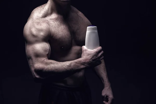 Красивый культурист с мускулистым телом держит бутылку шампуня — стоковое фото