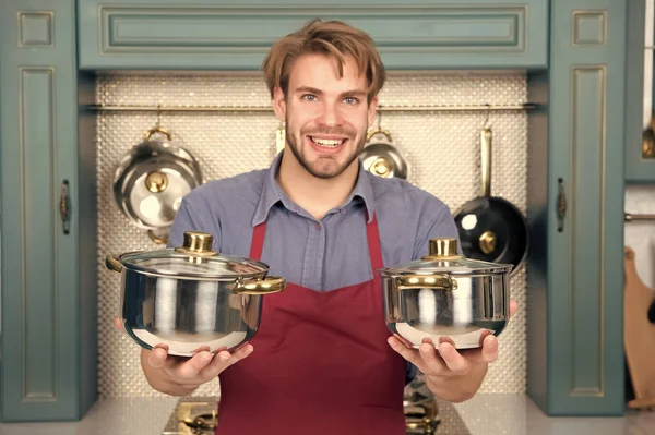 Кухонні горщики в руках щасливого чоловіка в червоному фартусі — стокове фото