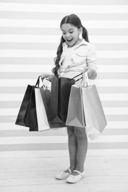 Alışveriş onun favori etkinliktir. Çocuk alışveriş torbaları çizgili arka plan taşır. Çocuk kız Satılık sezon tadını çıkarın. Kız gülümsemek yüz çanta tutan memnun. Çocuk heyecanlı hakkında okul için yeni giysiler satın