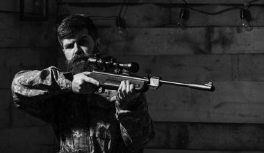 Sakallı kamuflaj elbiseler, ahşap iç arka plan giyer. Avcı, avcılık, kopya alanı daha önce silah nişan ile acımasız hipster. Avcı kavramı. Maço gamekeepers evinde sıkı yüzünde