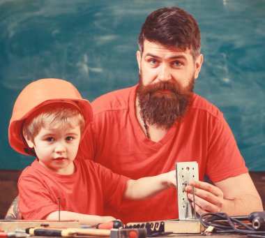 Küçük Yardımcısı kavramı. Sınıfta, arka plan kara tahta araçlarını kullanmak için küçük oğlu öğretim sakallı baba. Evlat, Çocuk koruyucu kask meşgul el ile baba ile onarım yapar