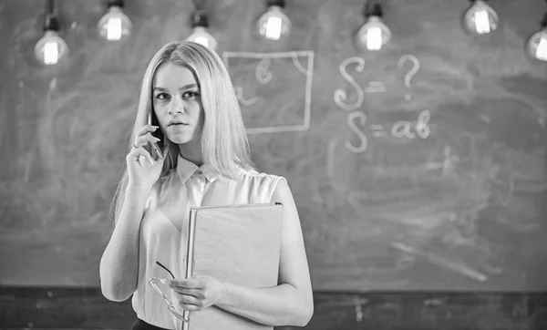 Conceito de relatório móvel. Mulher com livro falando no celular na sala de aula. Professor em problemas de resolução de face concentrada no telefone, quadro-negro no fundo. Professor relatando sobre alunos ausentes — Fotografia de Stock