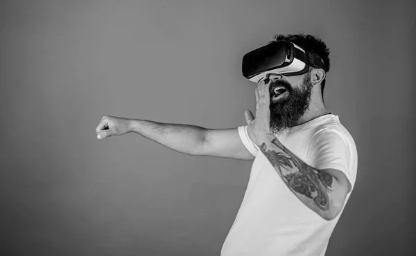 Man with beard in VR glasses driving car, red background. Virtual driving lessons concept. Hipster on happy face driving car and waving hand in virtual reality with modern digital gadget