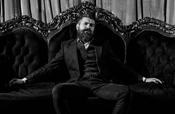 Millionaire in elegant suit sits on luxurious sofa. Bearded man with confident face in classic interior. Luxury lifestyle, confidence, success, rich, power, fashion, wealth, furniture, concep — Stock Photo, Image