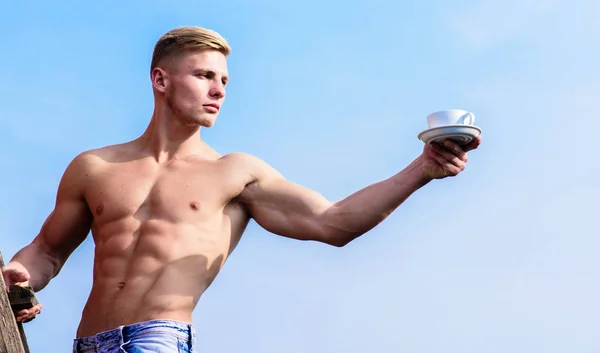 Sexy torso attractive waiter. Man muscular athlete bodybuilder offers you coffee. Macho muscular chest naked torso hold mug of fresh coffee blue sky background. Waiter bare chest hold coffee cup