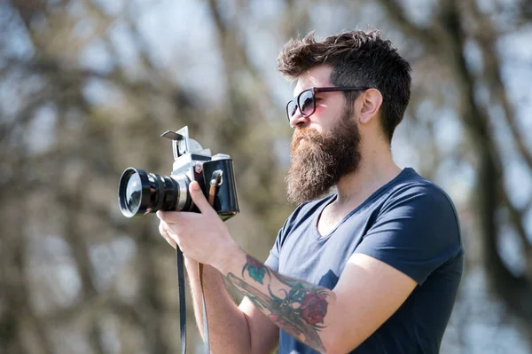 Hombre barbudo hipster fotógrafo mantenga la cámara vintage. Fotógrafo con barba y bigote fotógrafo aficionado fondo de la naturaleza. Un hombre con barba larga ocupado con fotos. Concepto de fotógrafo — Foto de Stock