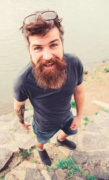 Hipster sur le visage joyeux avec des lunettes de soleil à la mode. Guy a l'air cool avec des lunettes de soleil élégantes. Concept de mode. Homme avec barbe et moustache porte des lunettes de soleil, surface de l'eau sur le fond — Photo