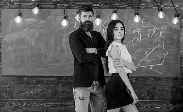 Conceito de parceiros. Homem com barba e sexy menina professor stand em sala de aula, quadro no fundo. A senhora e o hipster a trabalhar juntos na escola. Professor e rigoroso professor olhar confiante — Fotografia de Stock