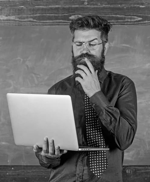 Distance education concept. Surfing internet. Hipster teacher wear eyeglasses and necktie holds laptop surfing internet. Teacher bearded man with modern laptop surfing internet chalkboard background — Stock Photo, Image