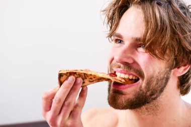 Genç adam evde çıplak ve pizzayla dinleniyor. Yatağında pizza olan gömleksiz genç bir adam. Diyet kimin umurunda. Pizza yatağı.