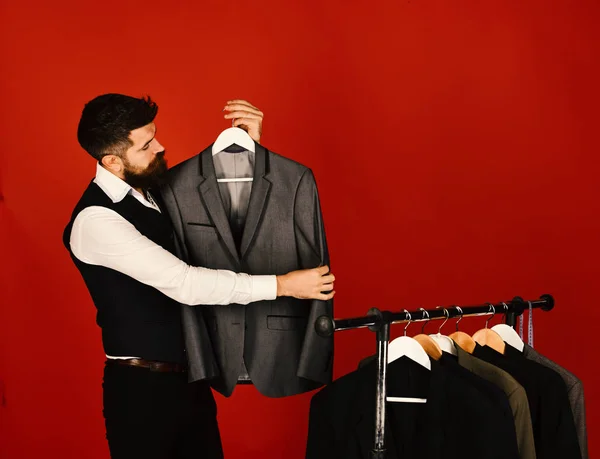 Asistente de tienda o vendedor sostiene traje gris en percha de ropa —  Fotos de Stock