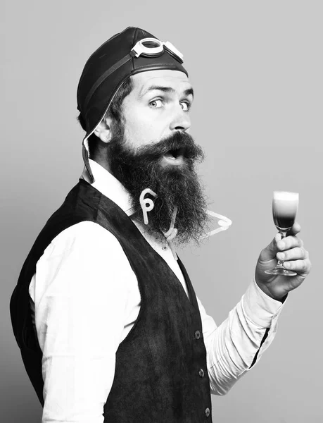 Yakışıklı sakallı pilot ya da uzun sakallı ve bıyıklı bir pilot elinde klasik süet deri yelek, mavi stüdyo arka planında şapka ve gözlüklü alkolik bardakları tutan komik bir adam. — Stok fotoğraf