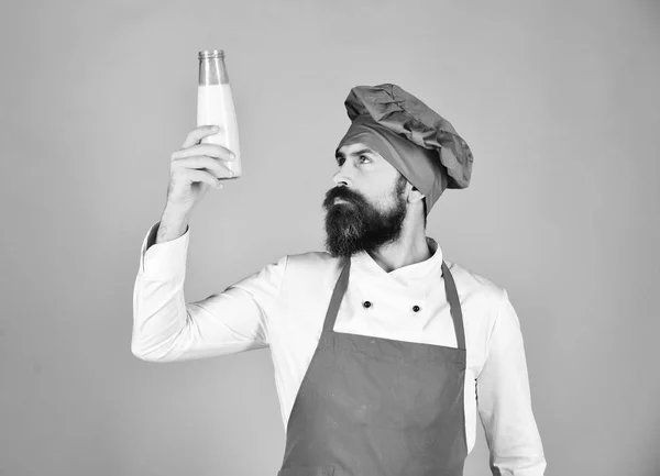 Koken met nieuwsgierig gezicht in bordeaux uniform houdt melk vast. — Stockfoto