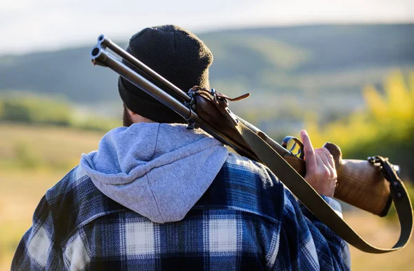 Hombre tipo brutal guardabosques en el fondo de la naturaleza sombrero. Brutalidad y masculinidad. Hunter lleva rifle en la mira trasera del hombro. Guy Hunter pasa tiempo libre cazando. Caza masculina hobby ocio concepto — Foto de Stock