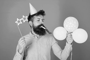 Hipster yıldız ile gözlük darbeler parti boynuz şeklinde. Sakin yüz sakallı adam hava balonları, mavi arka plan tutar. Sürpriz kavramı. Tatil öznitelikleri ile parti şapkalı adamı kutluyor