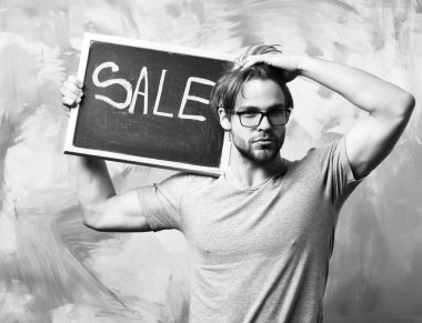 Beyaz sakallı seksi maço adam elinde satılık bir yazı tutuyor.