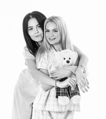 Sarılma, beyaz arka plan üzerinde izole kız. Kız ya da arkadaşlarım pijama ile peluş oyuncak ayı. Şirin kavramı. Sarışın ve esmer gülümseyen yüzler uyku giysileri üzerinde şirin ve samimi görünüyor