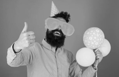 Sakal ve bıyık mutlu yüz tutan grup hava balonları, kırmızı arka plan üzerinde olan adam. Kutlama kavramı. Hippi dev güneş gözlüğü Doğum günü kutluyor. Parti şapkalı adamı yukarı hareketi gösterir