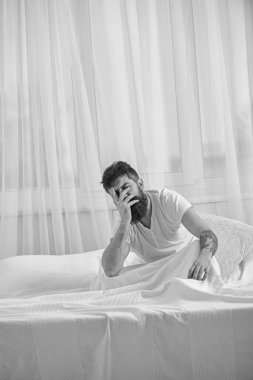 Akşamdan kalma kavramı. Adam sabah uyanma hayal kırıklığına acı yüzü. Sakal ve bıyık maço akşamdan kalma uğrar. Tişörtlü adam yatak uyanık, beyaz perde arka plan üzerinde oturur