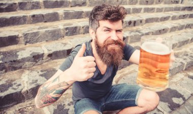 Sakal ve bıyık tutan cam bira ve gösterileri başparmak yukarı, taş merdivenle arka plan ile olan adam. Soğuk bir bira ile dinlenme adam. Cuma kavramı relax. Hipster neşeli yüz açık bira içmek