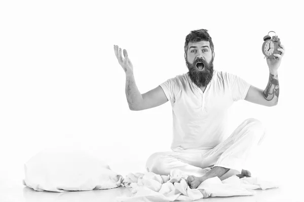 Homem com rosto chocado senta-se perto de travesseiro, mantém despertador . — Fotografia de Stock