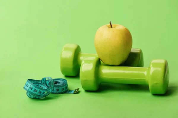 Haltères de couleur verte, ruban à mesurer torsadé et fruits — Photo