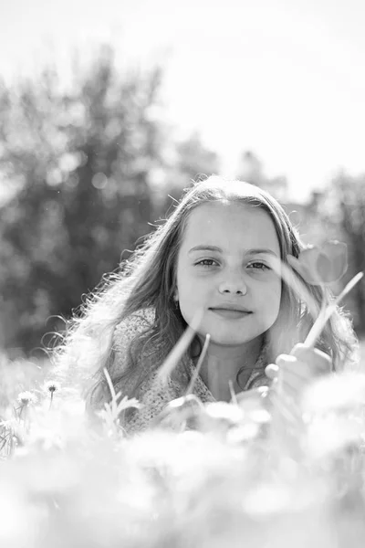 背景には、デフォーカスの自然草の上に横たわる少女。子供は、草原に横たわっている間春の晴れた日を楽しみます。季節性アレルギーの概念。笑顔の女の子が赤いチューリップの花を保持して、軽をお楽しみください。 — ストック写真
