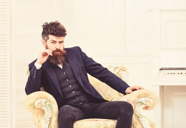 Macho atractivo y elegante en cara seria y expresión reflexiva. Concepto de estilo de vida Elite. Hombre con barba y bigote con traje clásico, se sienta en un sillón a la antigua, fondo blanco —  Fotos de Stock