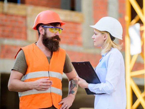 Woman engineer and bearded brutal builder discuss construction progress. Construction project management. Building industrial project. Construction industry concept. Discuss progress project