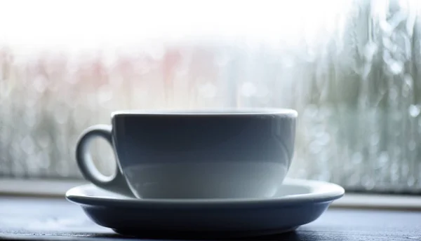Coffee time on rainy day. Wet glass window and cup of hot coffee. Autumn cloudy weather better with caffeine drink. Enjoying coffee on rainy day. Fresh brewed coffee in white cup or mug on windowsill