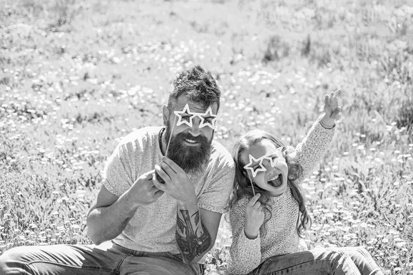 Rock star koncept. Far och dotter sitter på gräset på grassplot, grön bakgrund. Barn och pappa poserar med stjärna formad eyeglases foto monter attribut på ängen. Familjen tillbringar fritid utomhus — Stockfoto