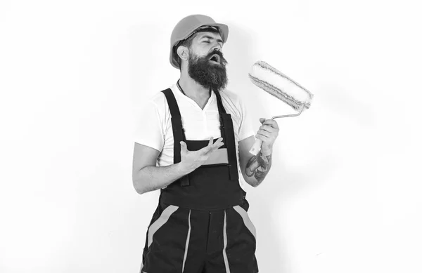 Fun at work. Builder holding paint roller as microphone. Young man singing lyric song over white background