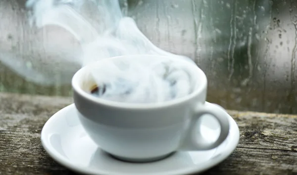 Autumn cloudy weather better with caffeine drink. Enjoying coffee on rainy day. Coffee time on rainy day. Fresh brewed coffee in white cup or mug on windowsill. Wet glass window and cup of hot coffee — Stock Photo, Image