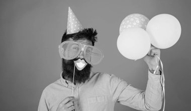 Hippi dev güneş gözlüğü kutluyor. Neşeli yüzündeki sakallı gülümseyen ağız sopa, kırmızı bir arka plan üzerinde tutar. Hava balonları ile parti şapkalı adamı kutluyor. Fotoğraf booth eğlence kavramı