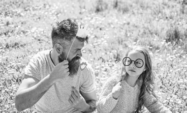 Baba ve kızı, grassplot, arka planı yeşil çimenlerin üzerinde oturur. Aile açık havada eğlence harcamak. Çocuk ve babası crown ve gözlük ile poz booth öznitelikleri fotoğraf. En iyi arkadaşlar kavramı