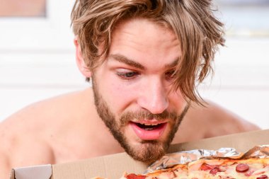 Seksi erkek yatakta yatarken pizza yemek. Evde yatakta lezzetli bir pizza yemek parlak bir apartman dairesinde öğrencidir. Adam yakışıklı bekar yatakta kahvaltı için peynirli yemek yeme sakallı. Pizza gibi insanlar.