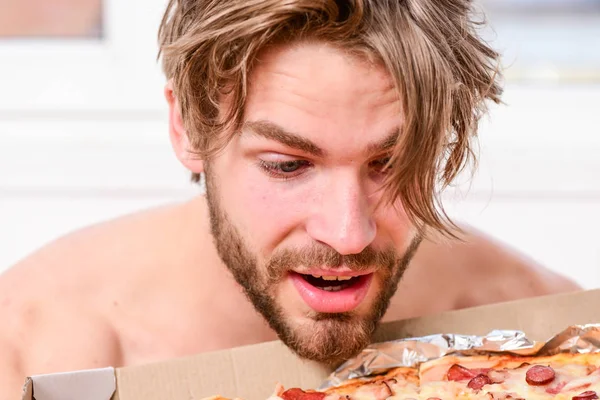 Sexy man zjeść pizzę, leżąc na łóżku. Student jest w domu na łóżku w jasne mieszkanie, jedzenie smaczne pizzy. Człowiek Brodaty przystojny kawaler, kiepskie jedzenie na śniadanie w łóżku. Ludzi takich jak pizza. — Zdjęcie stockowe