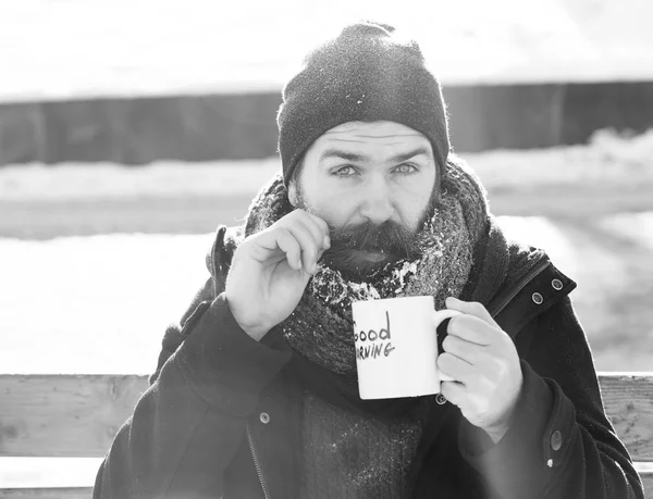 재미 있는 남자, 수염 및 콧수염과 수염된 hipster 덮여 흰 서 리 음료와 컵에서 좋은 아침 텍스트 자연 backgroun에 야외에서 눈 겨울 날에 나무 벤치에 앉아 — 스톡 사진