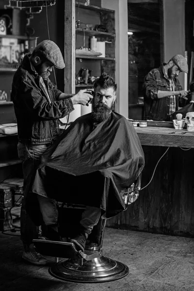 Un client hippie qui se fait couper les cheveux. Barbier avec tondeuse couper les cheveux sur le temple du client. Barbier avec tondeuse à cheveux travaille sur la coiffure pour barbe homme fond de salon de coiffure. Concept de style de vie Hipster — Photo