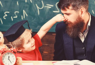 Baba sakallı, evlat, öğretmen öğretir burnunu pinching çocuk iken küçük çocuk. Öğretmen ve öğrenci kolej, kara tahta arka plan içinde. Neşeli oyun baba ile çocuk. Oynak çocuk kavramı
