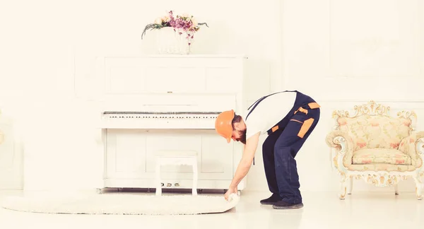 Verhuizen concept. Loader wrappes tapijt in roll. Man met de baard, worker in overalls en helm rollen tapijt, witte achtergrond. Koerier levert meubels in geval van verhuizing uit, verplaatsing — Stockfoto