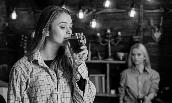 Friends enjoy mulled wine in warm atmosphere, wooden interior. Girls relaxing and drinking mulled wine. Friends on relaxed faces in plaid clothes relaxing, defocused. Rest and relax concept