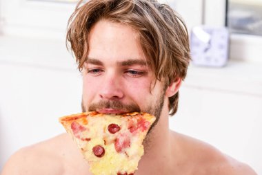Yakışıklı adam bir parça pizza elinde tutar ve bu yemek. Yatakta pizzayla gömleksiz yakışıklı genç adam. Ara diyet kavramı. Pizza gibi insanlar.