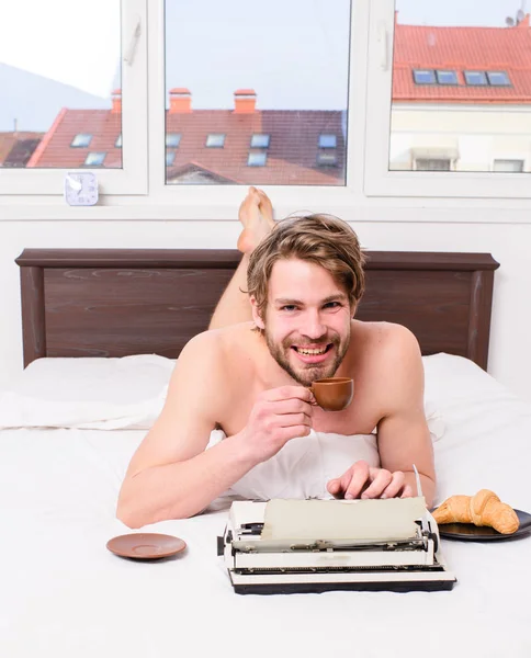 Szerző reggelizés ágy kávét iszik. Reggel ihletet. Kávé inspirálja őt, hogy írjon. Író romantikus szerző használt régi vágású írógép. Férfi író feküdt az ágy ágynemű dolgozó könyv — Stock Fotó