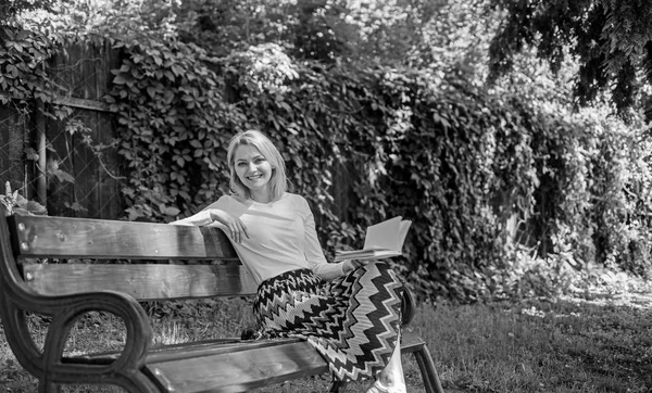 Signora godere di poesia in giardino. Goditi la rima. Donna felice sorridente bionda prendersi una pausa rilassante in giardino a leggere poesie. Ragazza seduta panchina rilassante con libro, sfondo verde natura. Poema romantico — Foto Stock