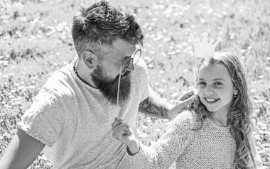 Baba ve kızı, grassplot, arka planı yeşil çimenlerin üzerinde oturur. Aile açık havada eğlence harcamak. Daddys Prenses kavramı. Çocuk ve babası crown ve gözlük ile poz booth öznitelikleri fotoğraf