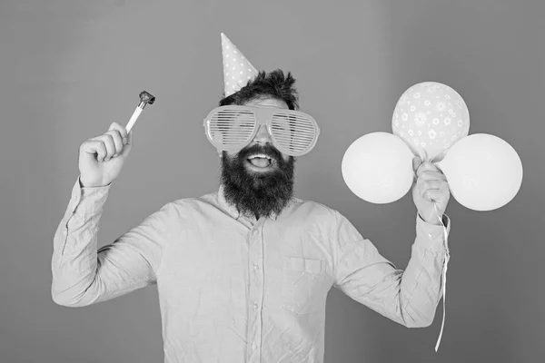 Mannen med skägg och mustasch på glada ansikte innehar luft ballonger, blå bakgrund. Party koncept. Hipster i giant glasögon firar födelsedag. Killen i partiet hatt med semester attribut firar — Stockfoto